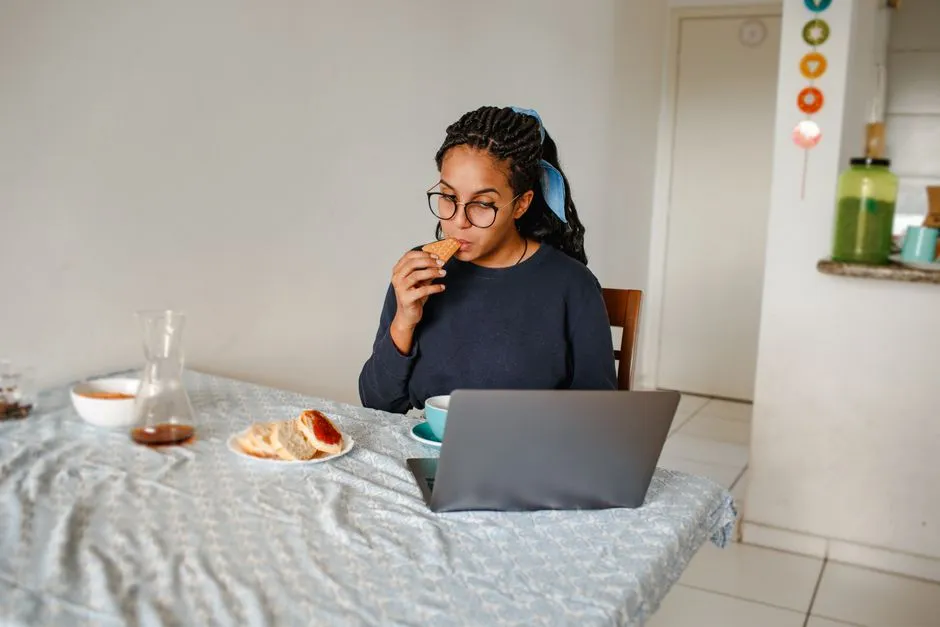 Person at a kitchen table working through a puzzle on a laptop with a mug going cold beside it